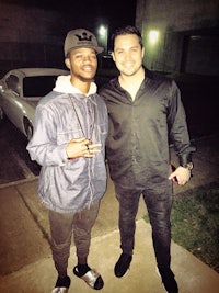 two men standing next to each other in front of a car