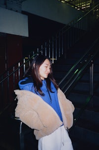 a woman in a blue jacket leaning against an escalator