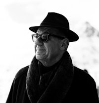 a black and white photo of an older man wearing a hat and scarf