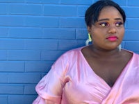 a black woman in a pink dress leaning against a brick wall