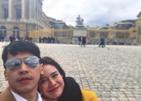 a man and woman posing for a selfie in front of a palace