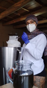 a woman wearing a mask and gloves in front of a large pot