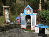a small shrine in the woods with a statue of st michael