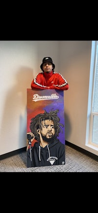 a man holding up a painting of a man with dreadlocks
