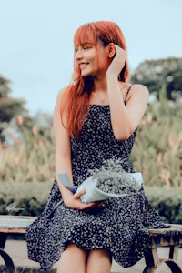 a woman with red hair sitting on a bench holding flowers