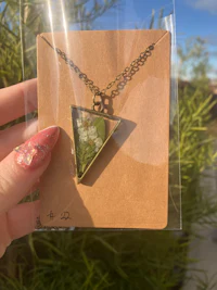 a person holding a necklace with a green triangle on it