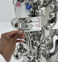 a person holding up a metal sculpture with balls on it