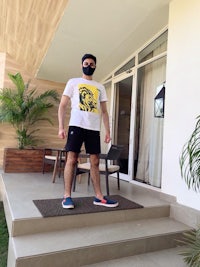 a man wearing a white t - shirt standing on the steps of a house