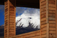 a snow covered mountain seen through a wooden window