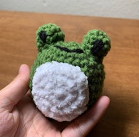 a crocheted frog stuffed animal is held in a hand