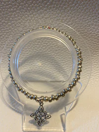 a silver beaded bracelet on a clear stand