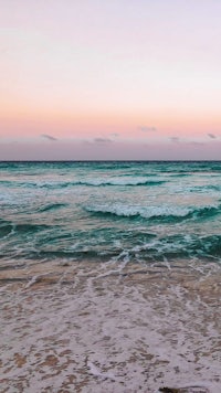 a beach with waves and a pink sky at sunset
