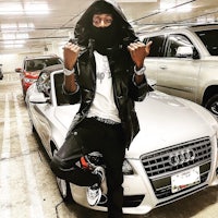 a man in a black hoodie standing next to a white audi