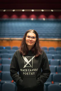 a woman in a black hoodie standing in front of an auditorium