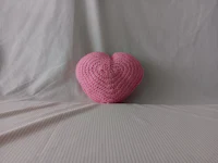 a pink heart shaped crocheted pillow on a white background