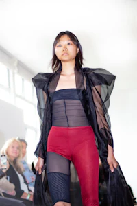 a woman walks down a runway wearing a black top and red pants