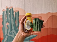 a hand holding a bottle of honey and a cactus