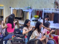 a group of women are sitting in a room with a lot of clothes