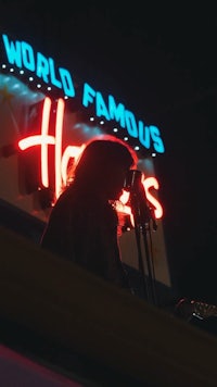 a man sitting on a balcony with a neon sign that says world famous harveys