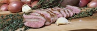 a piece of meat on a cutting board with onions and herbs