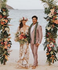 a bride and groom standing under a tropical wedding arch on the beach