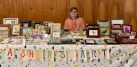 a woman standing in front of a table full of art