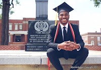 a man in a graduation cap and gown sits on a bench in front of a monument