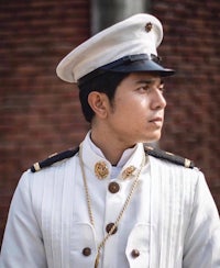 a young man in a white uniform standing in front of a brick wall