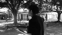 black and white photo of a boy playing a guitar in a park