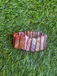 a bracelet made of red and brown pieces of mother of pearl laying on the grass