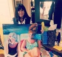 a woman holding up a painting of a woman in a bikini