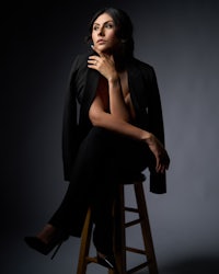 a woman in a black suit sitting on a stool