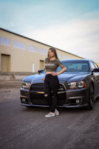a woman posing next to a gray dodge charger