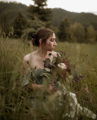 a woman sitting in a field holding a bouquet