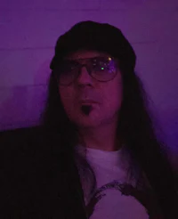 a man wearing glasses and a hat in front of a purple light