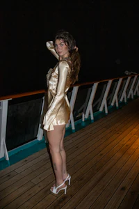 a woman in a gold dress standing on the deck of a cruise ship