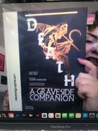 a woman holding up a book with the title death a graveside companion