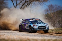 a blue and purple rally car driving down a dirt road