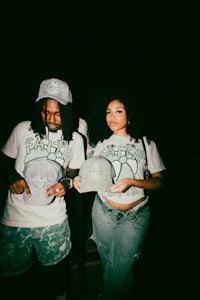 two people standing next to each other holding hats