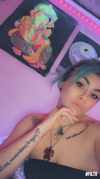 a woman with blue hair and tattoos posing in front of a pink wall