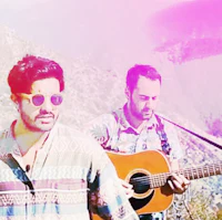 two men standing in front of a mountain with an acoustic guitar