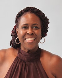 a black woman smiling in a brown top
