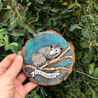 a person is holding a piece of wood with an opossum on it