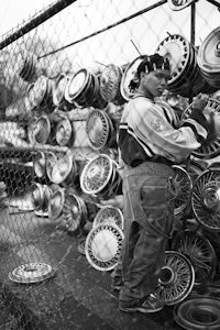 a black and white photo of a man standing next to a pile of car parts