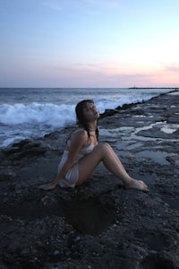 a woman sitting on rocks near the ocean