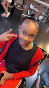 a young girl sitting in a hair salon making a peace sign