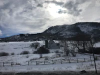 a snowy field with a fence and mountains in the background
