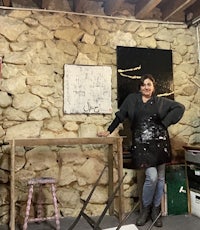 a woman standing in front of a stone wall in an art studio