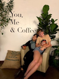 two women sitting in a chair next to a sign that says you me & coffee