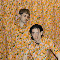 two men in floral shirts posing in front of a curtain